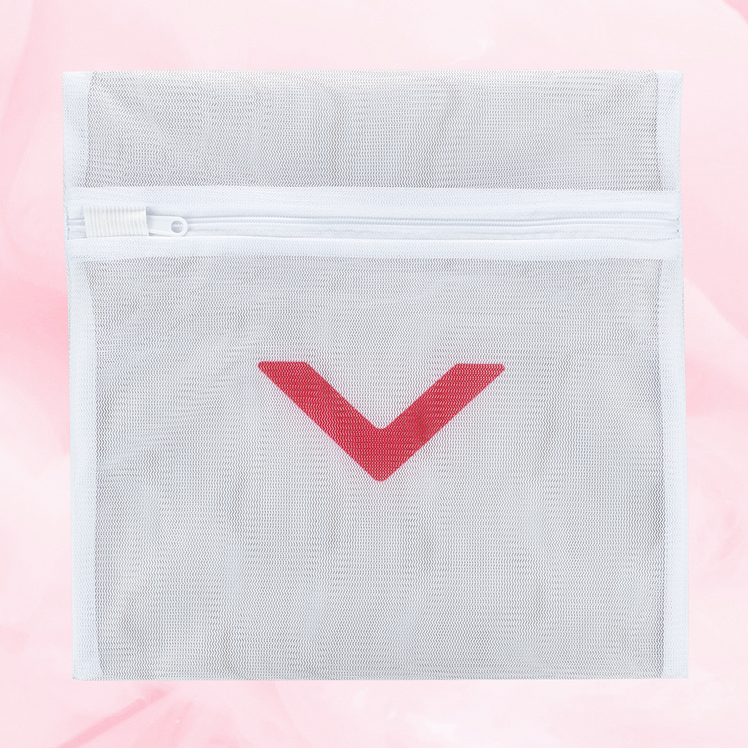 Pesupussi, valkoinen verkkopussi punaisella V-kuviolla, vetoketju päällä.