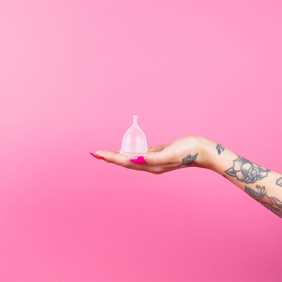 Käsi pitelee Kuukautiskuppia kirkasta taustaa vasten.