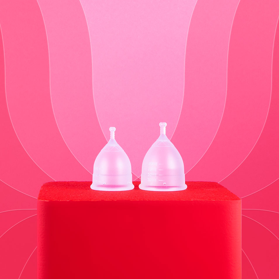 Kaksi läpikuultavaa Kuukautiskuppia punaisella alustalla.